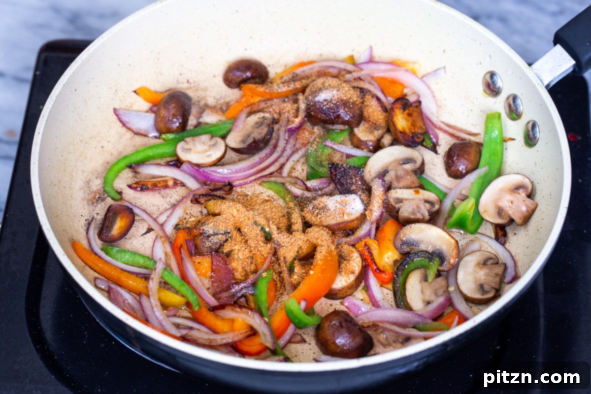 A colorful medley of sliced mushrooms, bell peppers, and onions sizzles in a skillet, now seasoned with a sprinkle of black pepper, taco spice, and additional salt. The spices lightly coat the vegetables as they sauté.