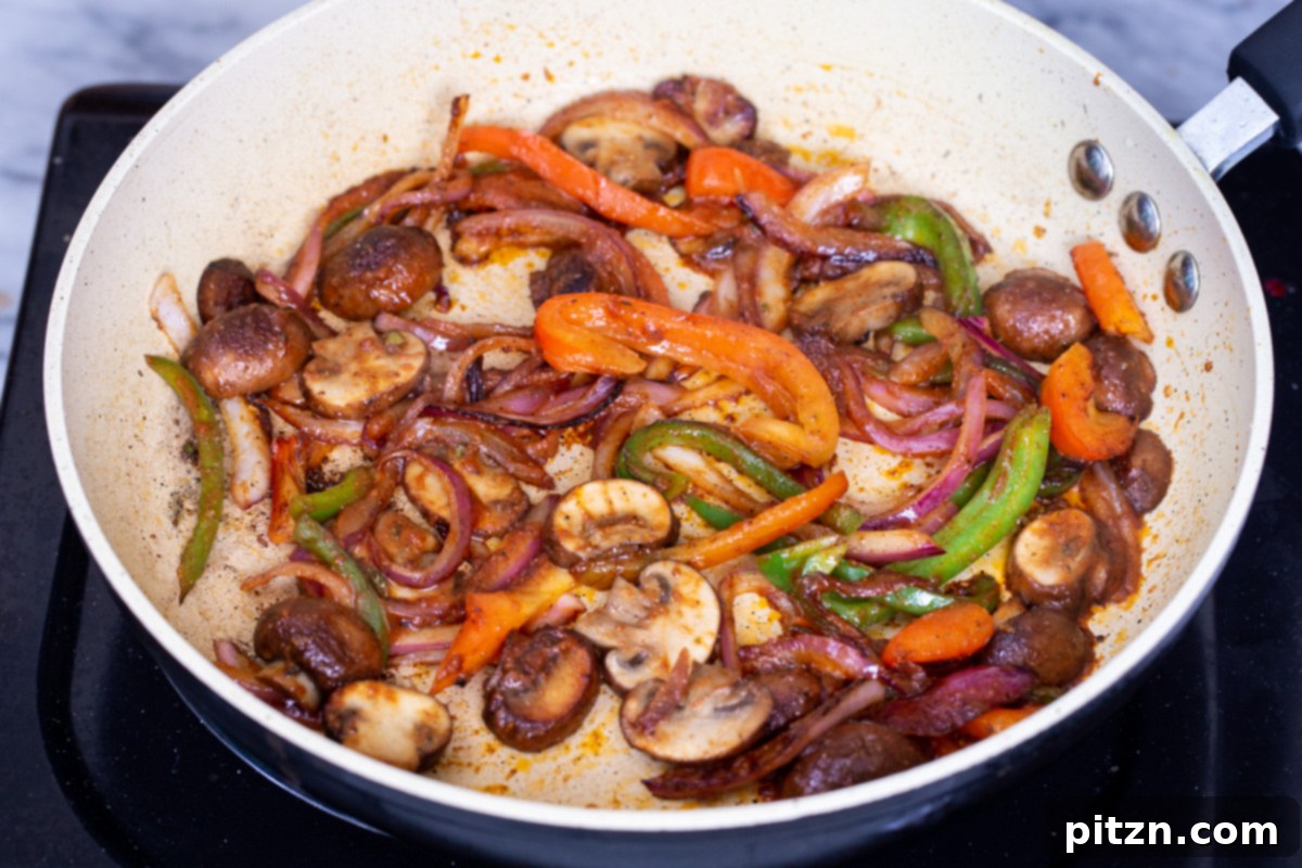 A skillet full of perfectly sautéed vegetables, including golden-brown mushrooms, tender bell peppers, and soft onions, now cooked down and ready as the flavorful filling for the vegan birria tacos.