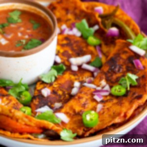 A close-up of a perfectly cooked Vegan Tikka Masala Birria Taco, showing its golden-brown tortilla and a peek of the flavorful filling. A small dish of the rich Tikka Masala sauce is in the background, ready for dipping.