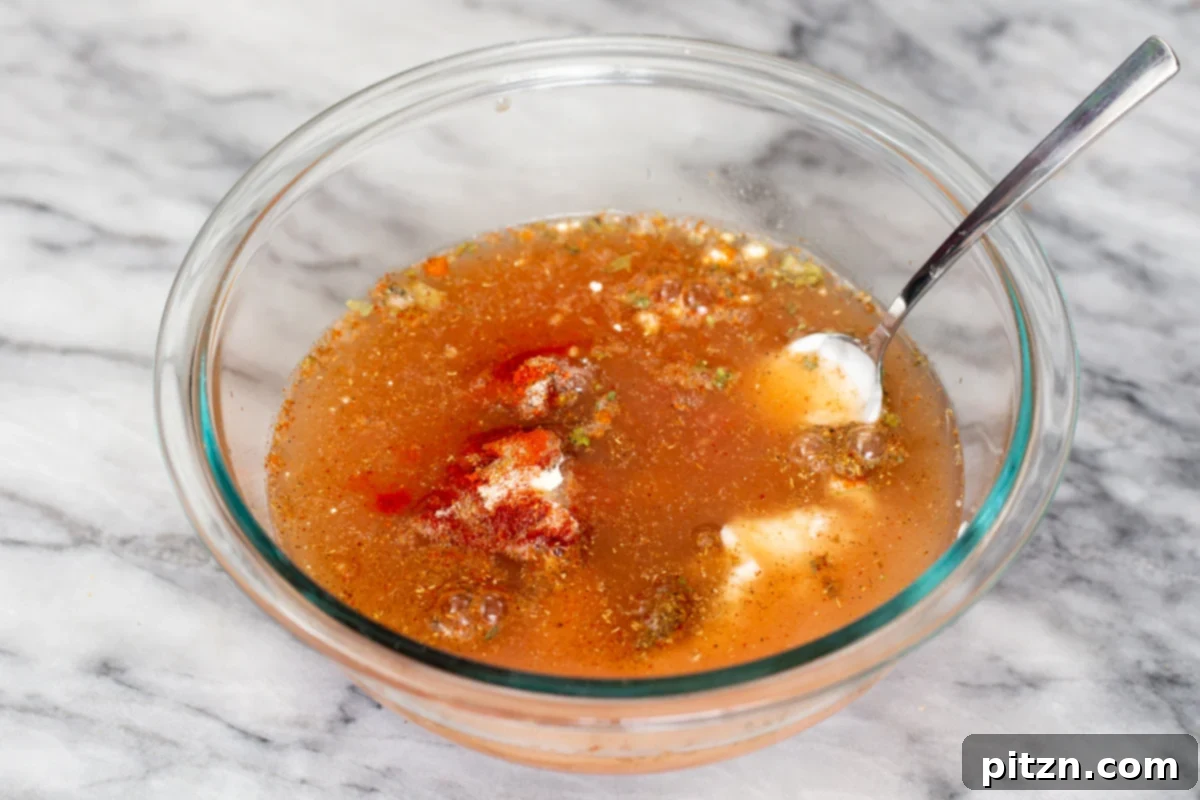Various ingredients for the Tikka Masala sauce, including spices, tomato paste, and a liquid component, are being actively combined in a small glass dish with a spoon. The vibrant colors of the mixture suggest a rich flavor profile in the making.