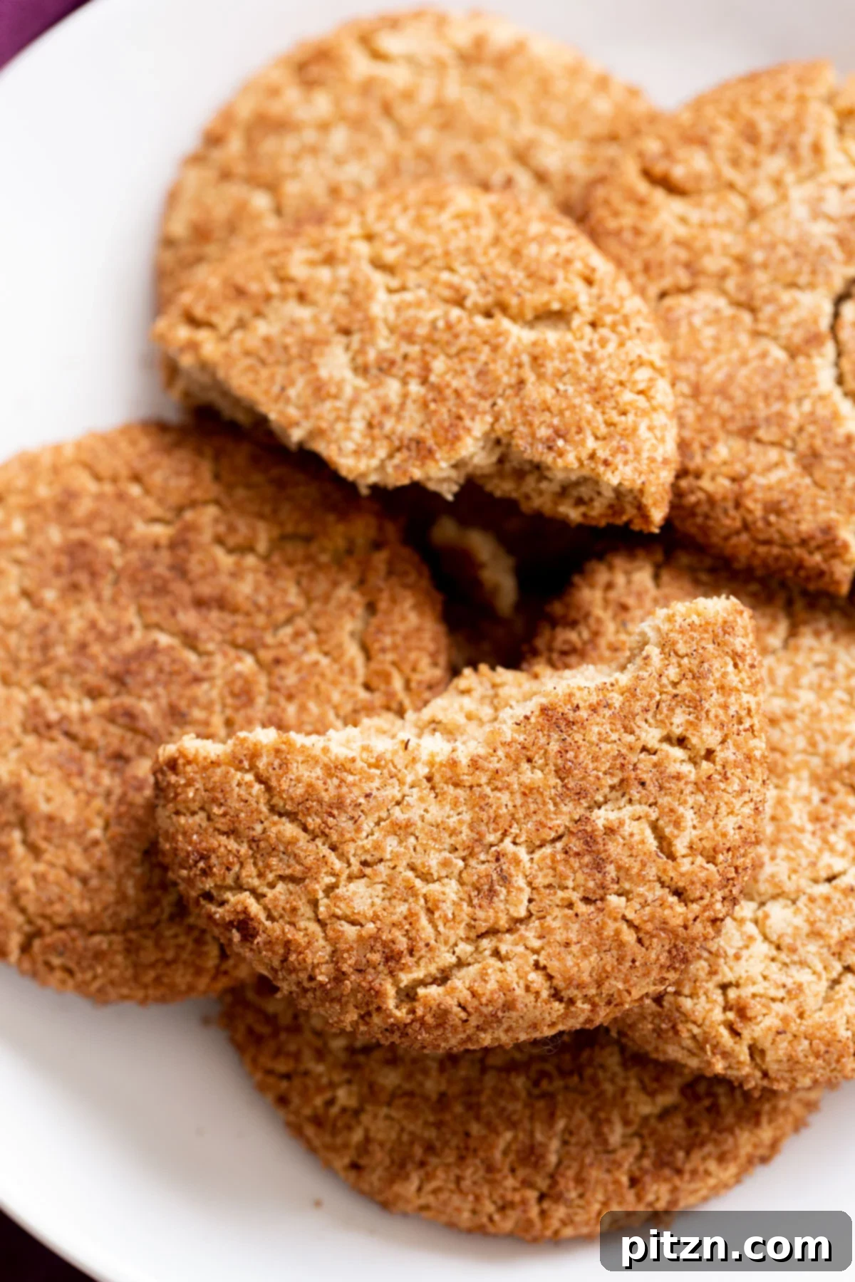 Soft and Chewy Gluten-Free Almond Flour Snickerdoodles 3 A close-up view of a platter with vegan gluten-free snickerdoodles, with one cookie expertly broken in half to reveal its soft, tender interior.