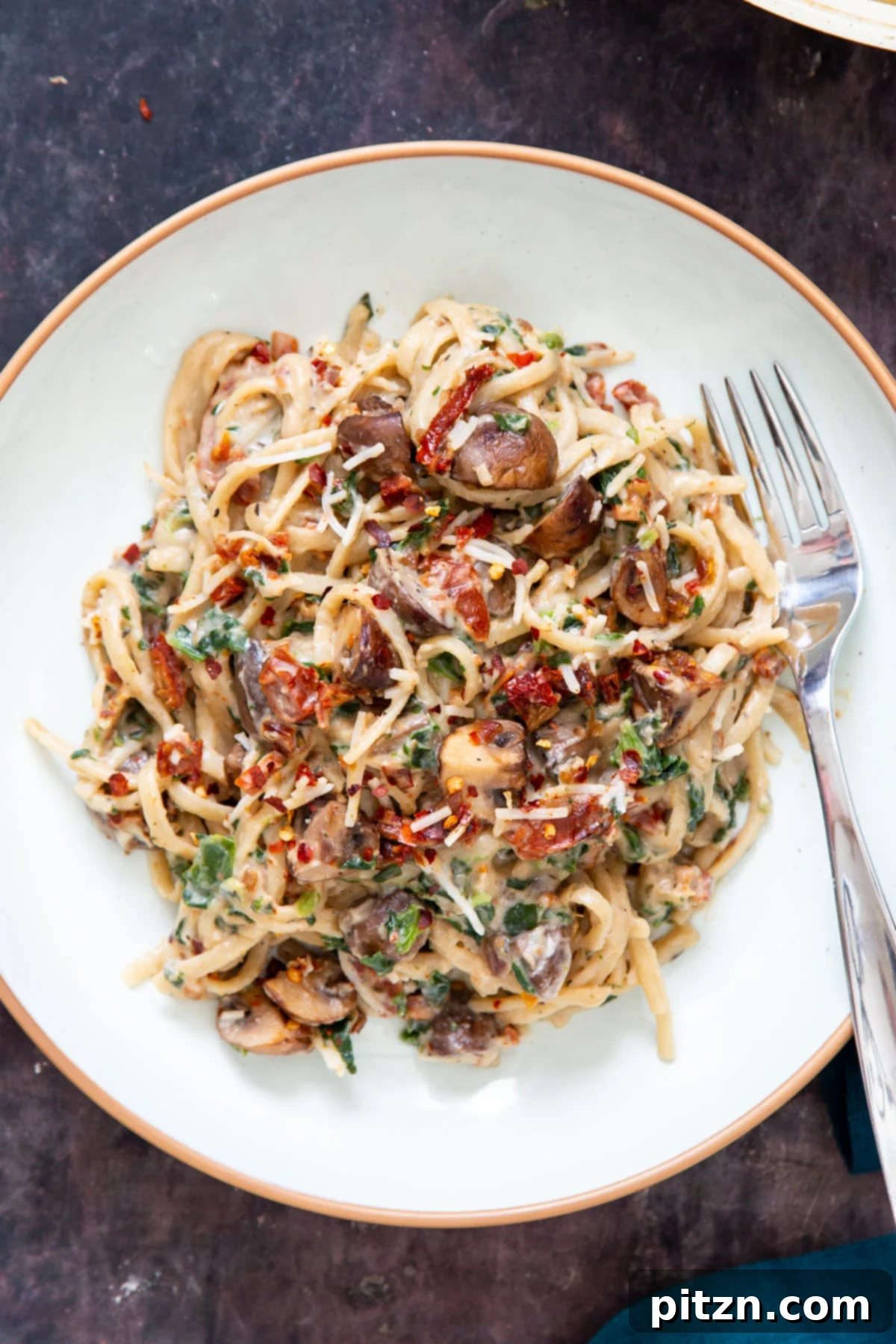 Creamy Vegan One-Pot Pasta: Mushrooms & Sun-Dried Tomatoes 2 A plate with creamy vegan one pot mushroom pasta with spinach and sun-dried tomatoes, garnished with fresh herbs and a sprinkle of vegan parmesan.