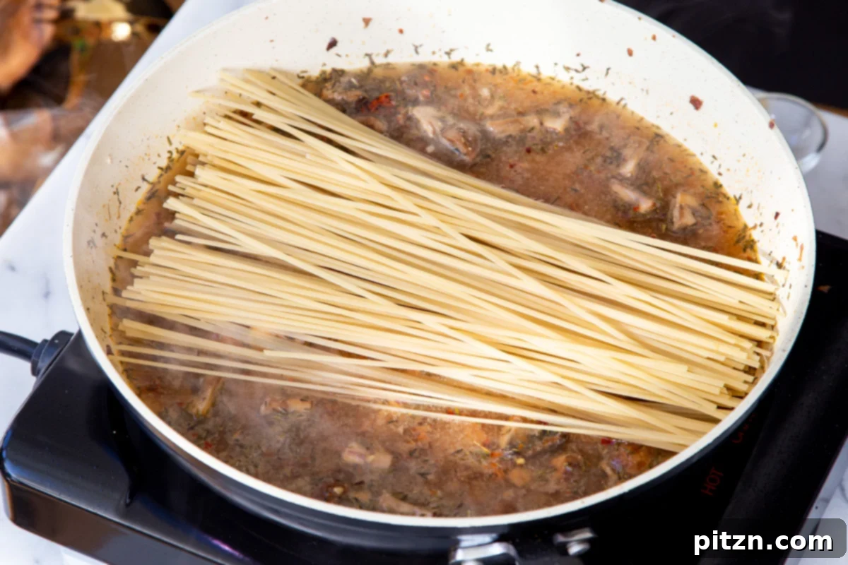 Creamy Vegan One-Pot Pasta: Mushrooms & Sun-Dried Tomatoes 14 Dried fettuccine pasta being carefully added to the pot with the simmering mushroom and sun-dried tomato sauce, ready to cook.