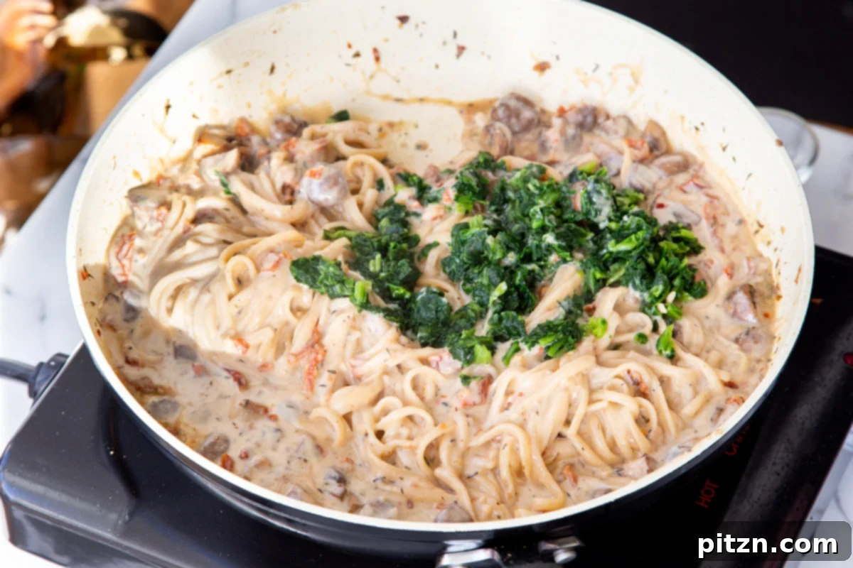 Creamy Vegan One-Pot Pasta: Mushrooms & Sun-Dried Tomatoes 18 Fresh spinach being folded into the creamy mushroom and sun-dried tomato pasta, adding a vibrant green and healthy touch.