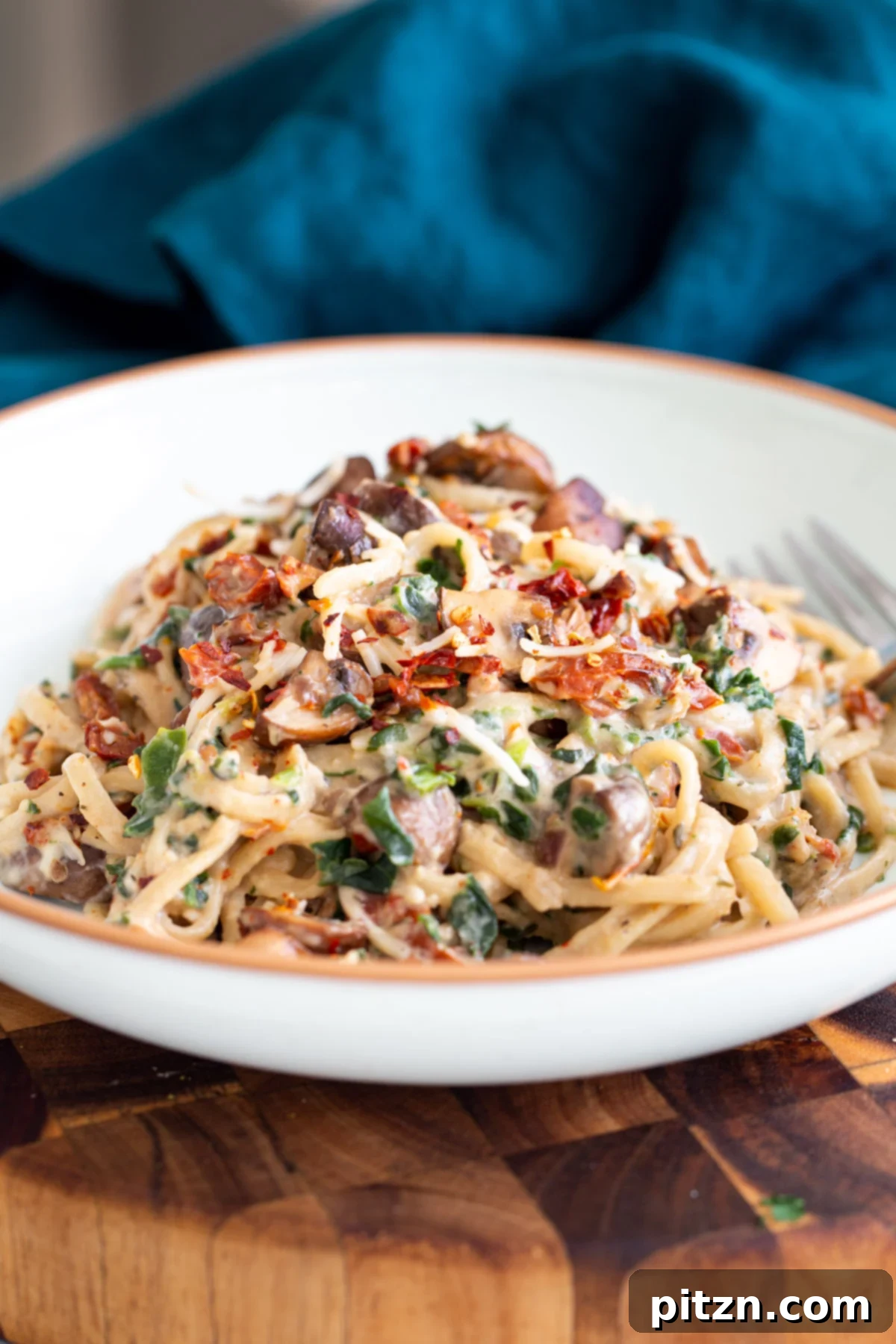 Creamy Vegan One-Pot Pasta: Mushrooms & Sun-Dried Tomatoes 3 Side view of creamy vegan mushroom pasta, generously topped with sun-dried tomatoes and fresh basil, showcasing its rich texture.