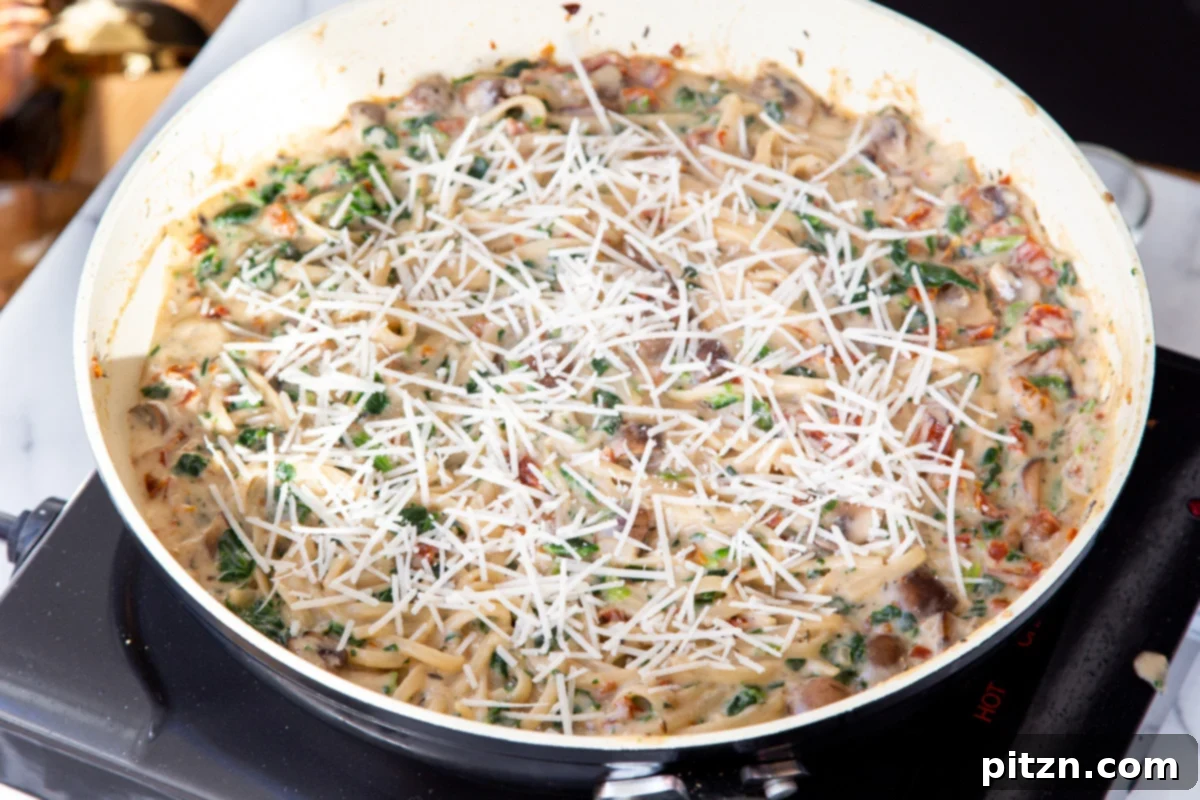 Creamy Vegan One-Pot Pasta: Mushrooms & Sun-Dried Tomatoes 20 Creamy spinach, mushroom, and tomato pasta in a saucepan, topped with a generous sprinkle of vegan shredded cheese, ready to melt.