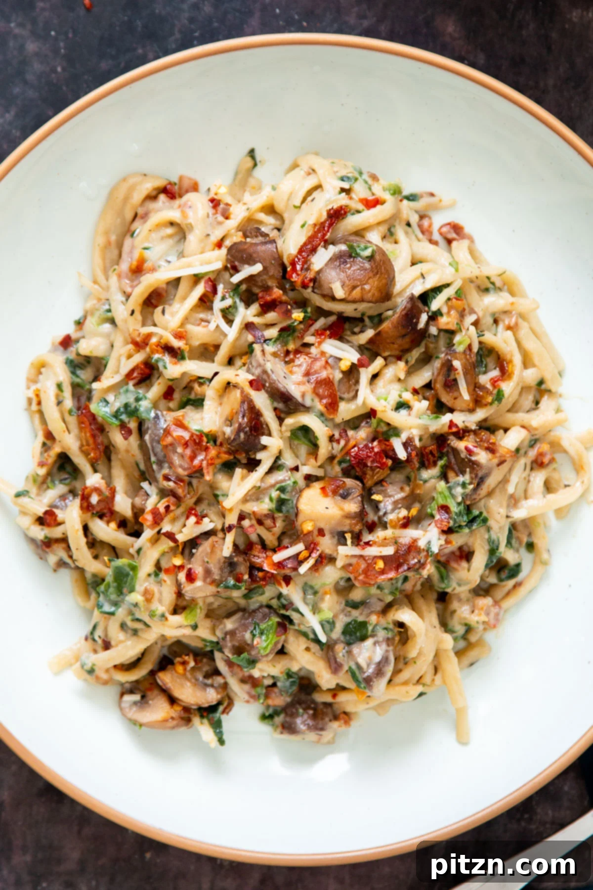 Creamy Vegan One-Pot Pasta: Mushrooms & Sun-Dried Tomatoes 22 A vibrant plate of one-pot vegan creamy mushroom pasta, adorned with spinach and sun-dried tomatoes, ready for a delicious meal.