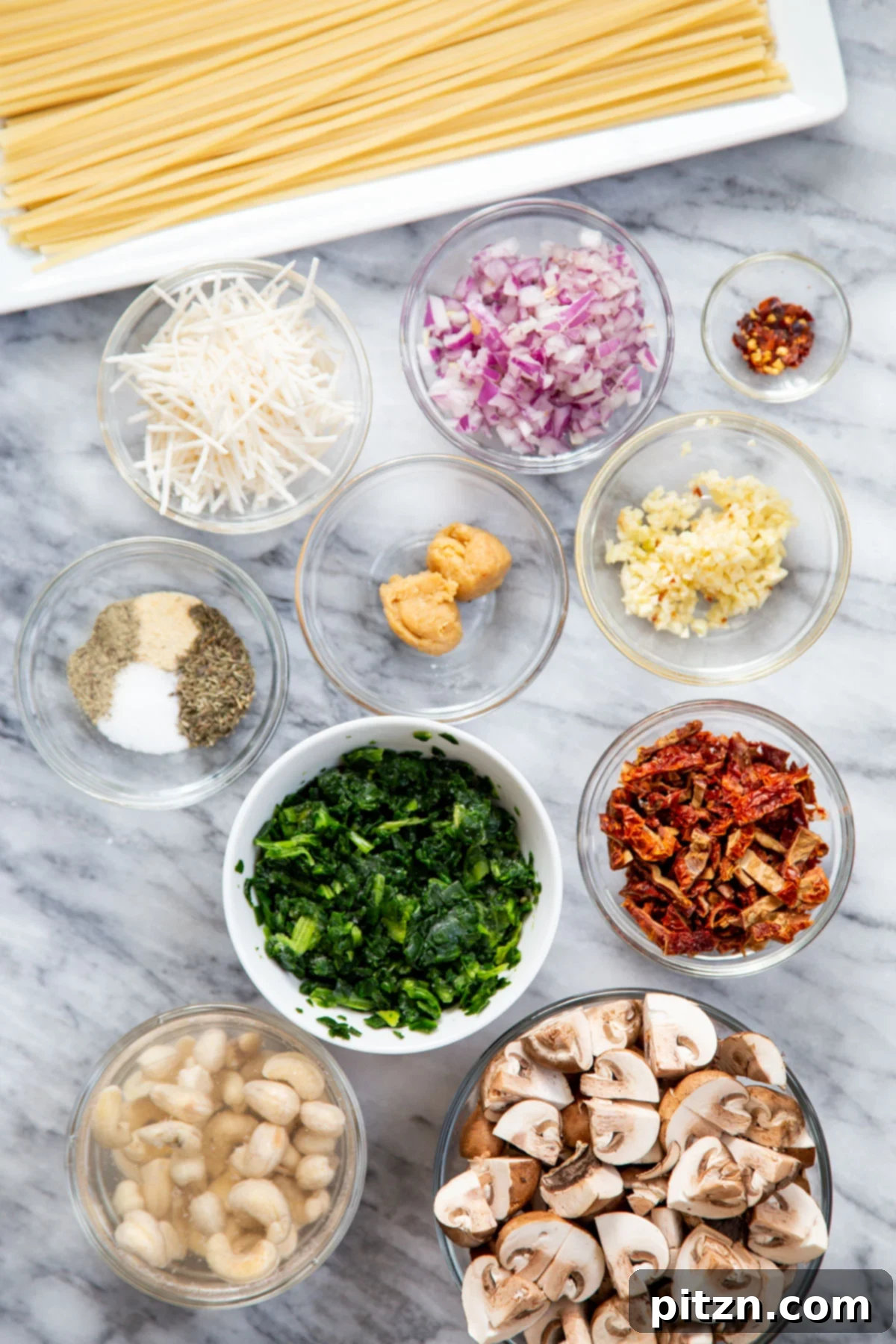 Creamy Vegan One-Pot Pasta: Mushrooms & Sun-Dried Tomatoes 6 Ingredients neatly laid out on a countertop, including pasta, mushrooms, sun-dried tomatoes, spinach, garlic, onion, and spices, ready for making creamy vegan mushroom pasta.