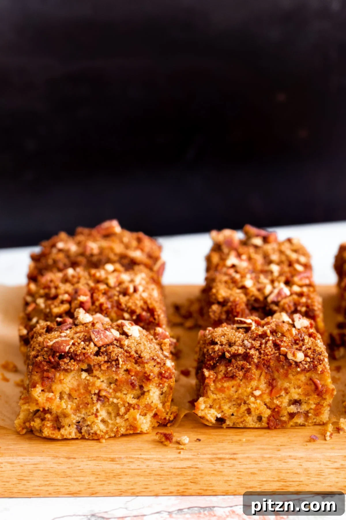 Spiced Vegan Carrot Cake Squares 5 Vegan carrot cake bars on a wooden board against a black background