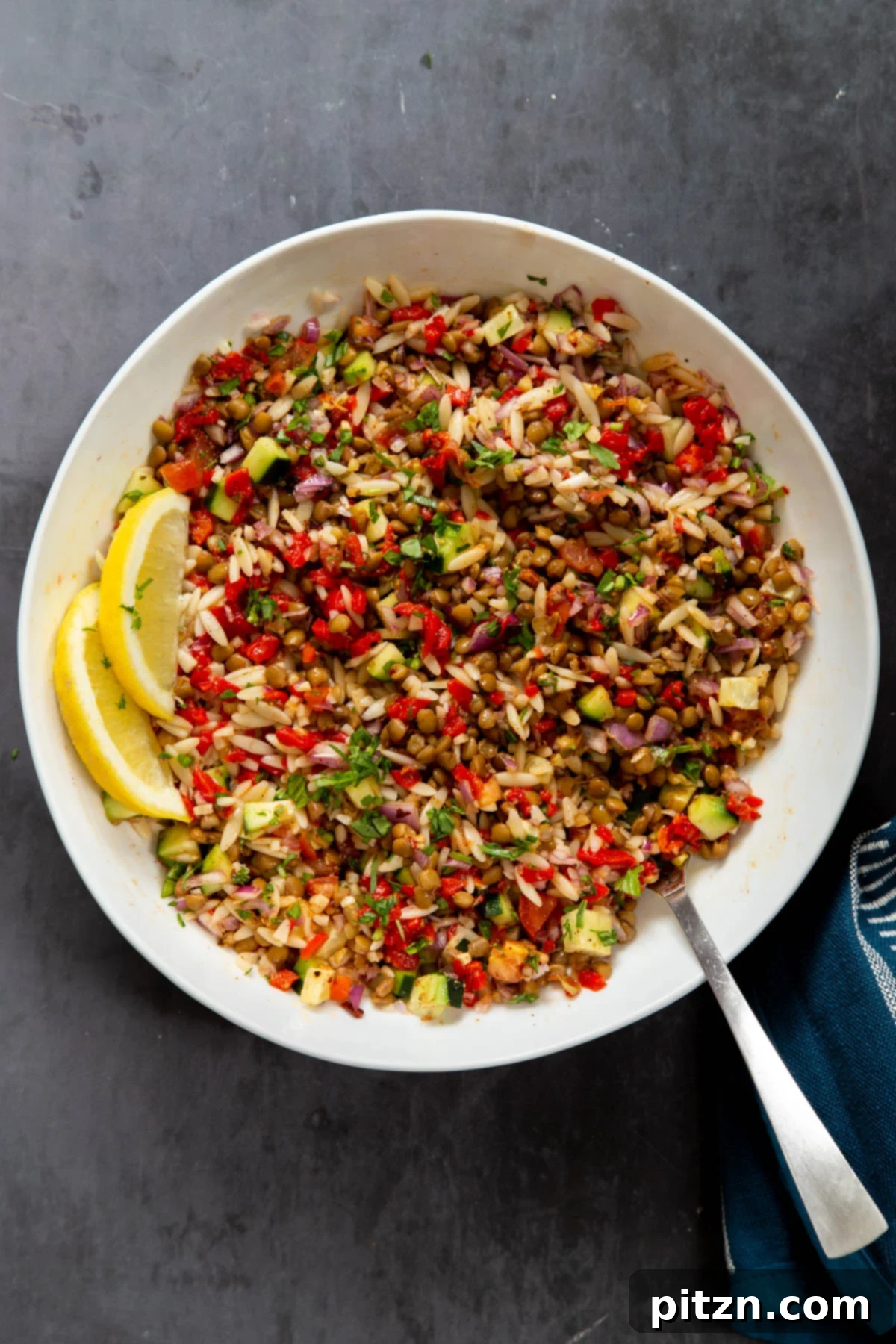 A close-up view of a large white bowl filled with vegan farro and lentil salad, featuring fresh vegetables and a glistening lemon-olive oil dressing, ready for serving.