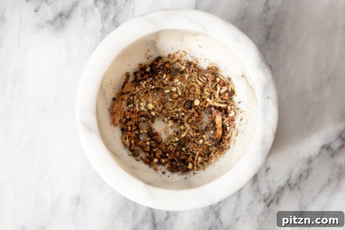 A small dish holding a fragrant assortment of freshly crushed whole spices, ready to be added to the curry base.