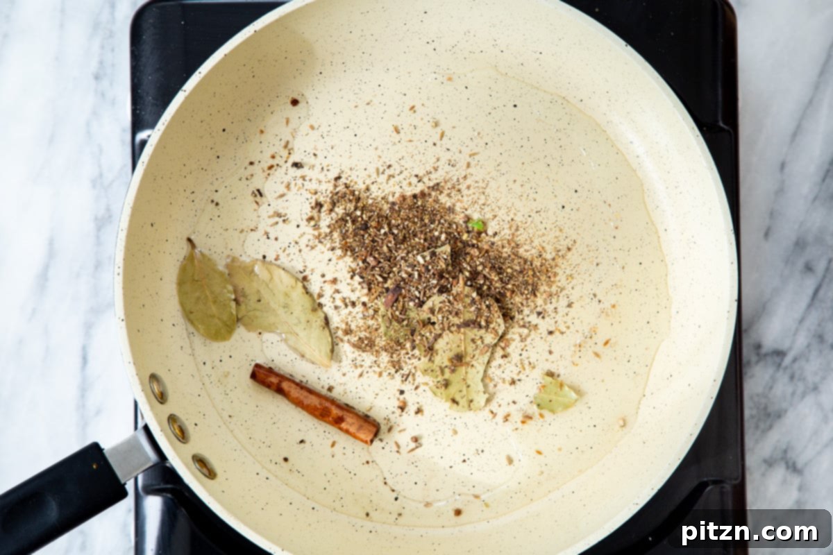 A frying pan filled with hot oil, infused with the rich aromas of whole spices as they are tempered.