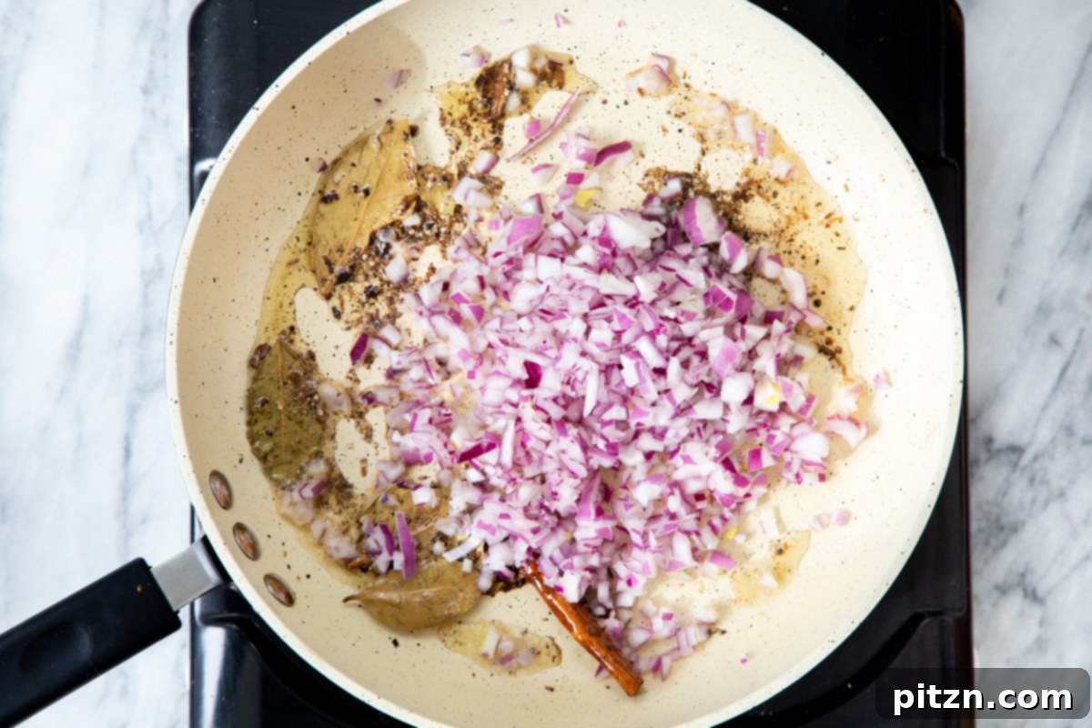 Finely chopped red onion being added to the frying pan, joining the aromatic tempered spices.