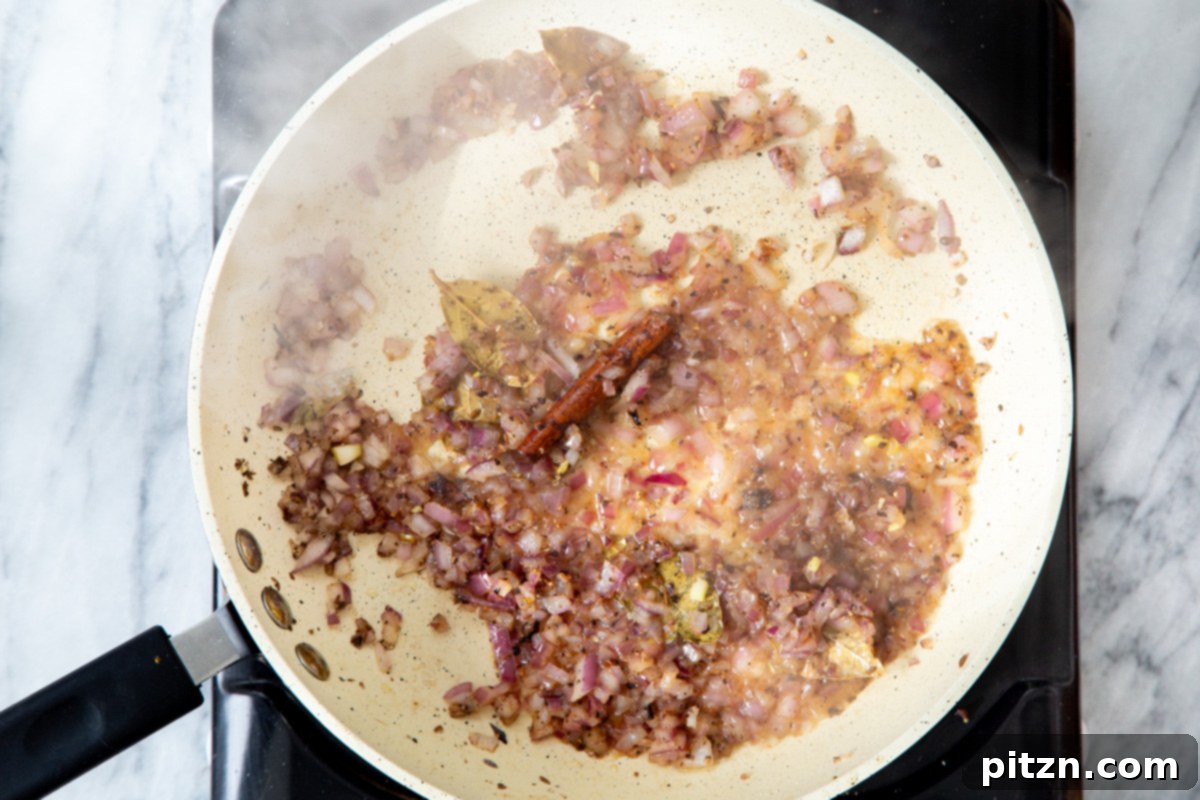 A close-up of sautéed onions and whole Indian spices mingling in a pan, creating a fragrant base for the curry.