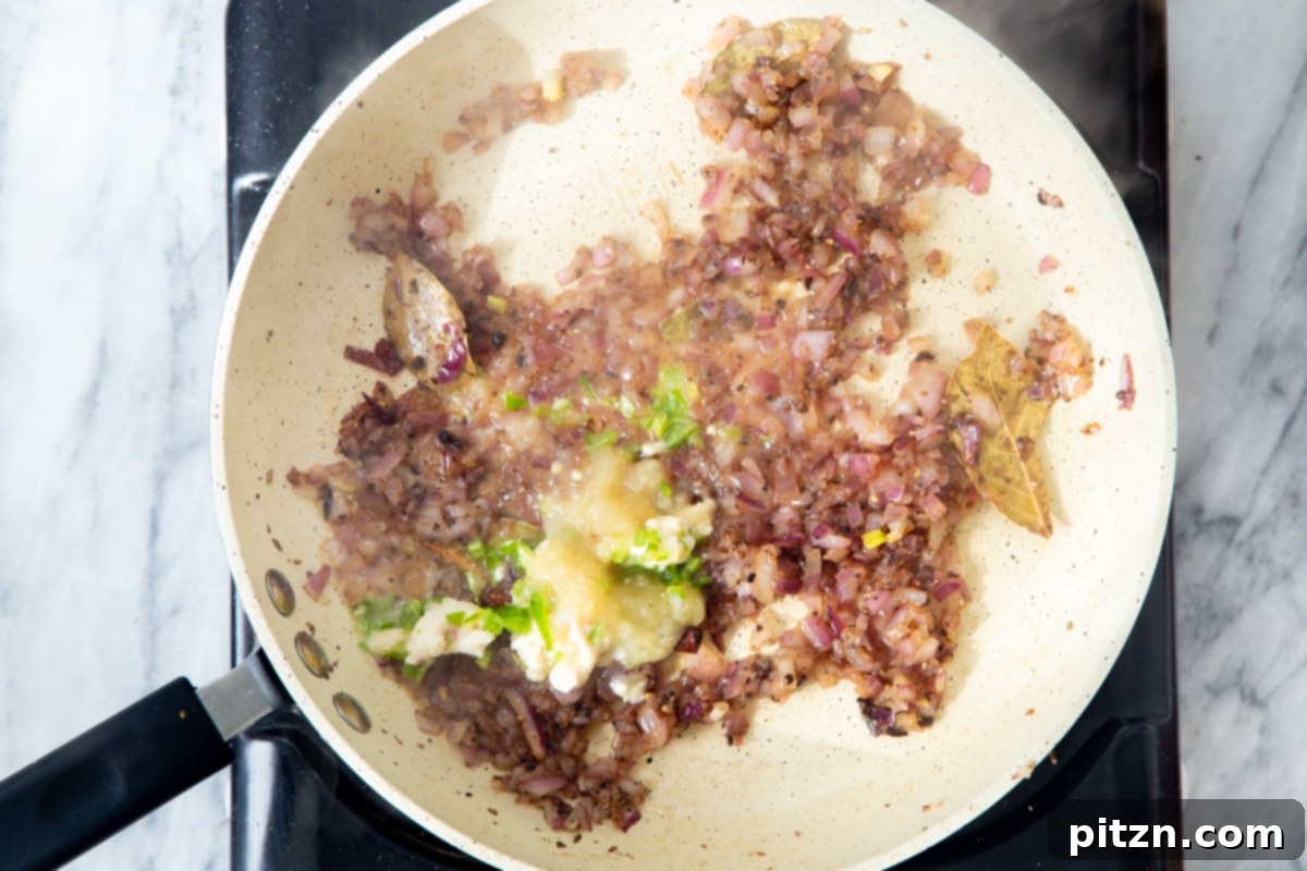 Ginger garlic paste being introduced to the sautéed onions and tempered Indian spices in the frying pan.