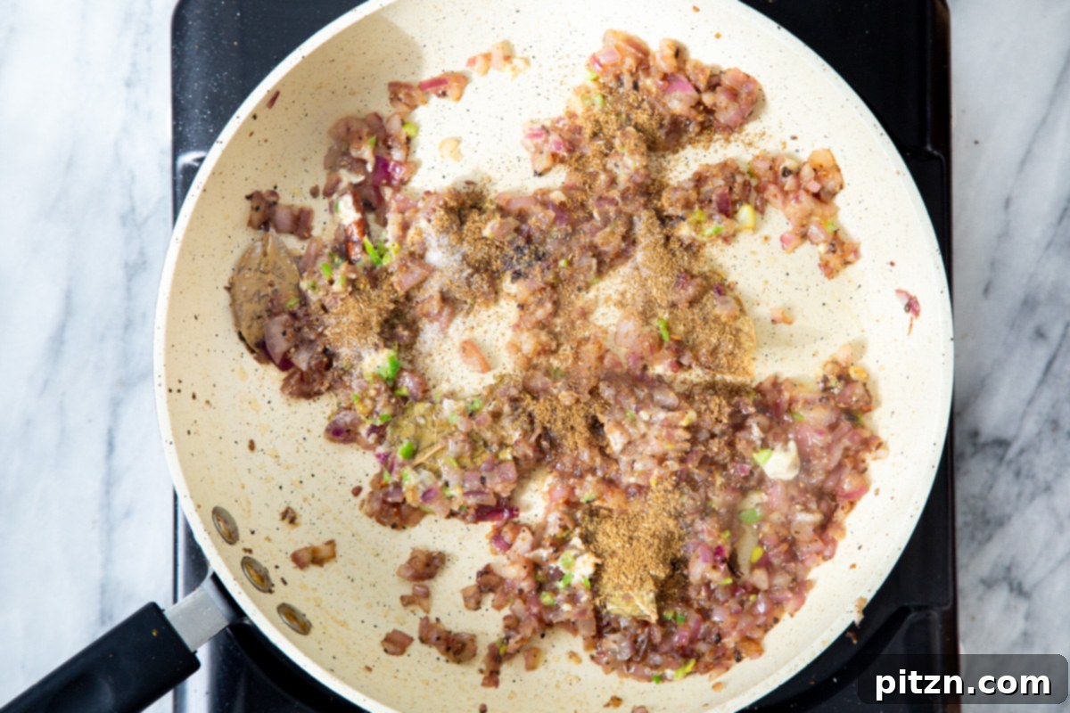 Ground spices, including garam masala and chili powder, being sprinkled over the aromatic base in the frying pan.