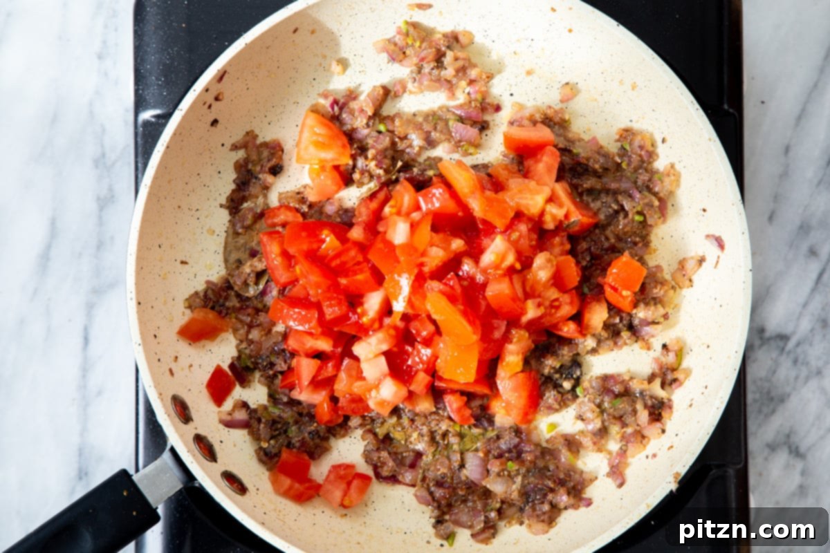 Chopped fresh tomatoes being added to the frying pan, joining the spiced onion mixture to form the rich gravy.