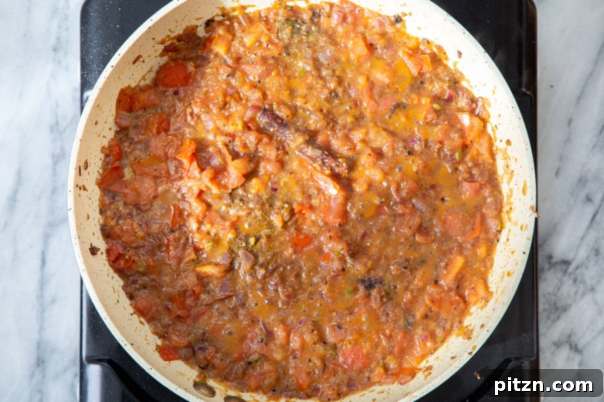 A rich, red Indian tomato gravy simmering to perfection in a frying pan, its texture thickening beautifully.