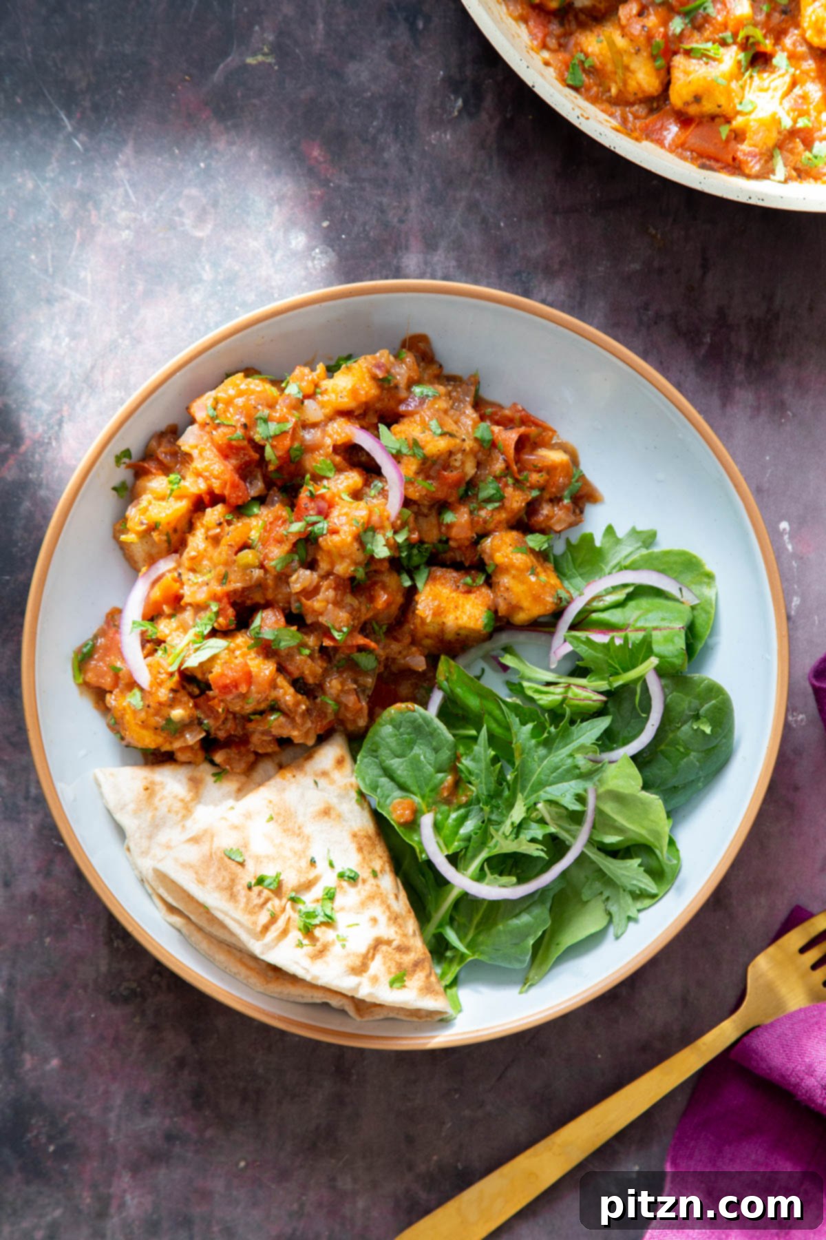 Close-up of a serving of baked tofu curry, accompanied by a fresh side salad and warm flatbread, with a golden fork poised for dining.