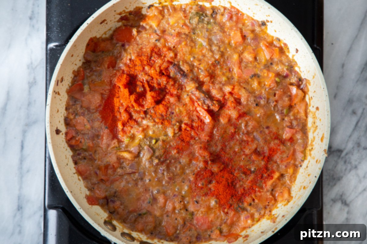 Additional chili powder and paprika being added to the simmering gravy in the frying pan, enhancing its color and spice.