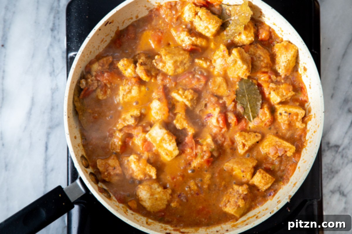 The finished Khada Masala Murg Curry with Baked Tofu, simmering briefly on a cooking plate within a sautéing pan, absorbing the rich flavors.