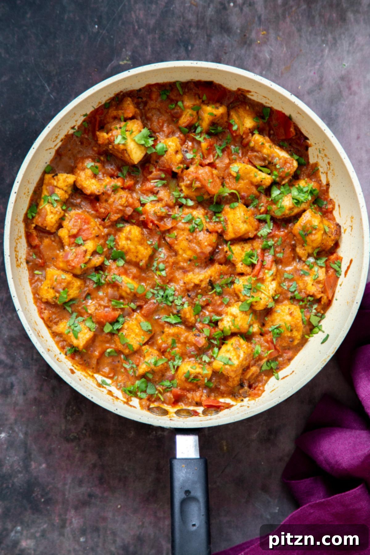 An overhead shot of a sautéing pan filled with Vegan Khada Masala Murg Curry and Baked Tofu, beautifully garnished with fresh cilantro, ready to be enjoyed.