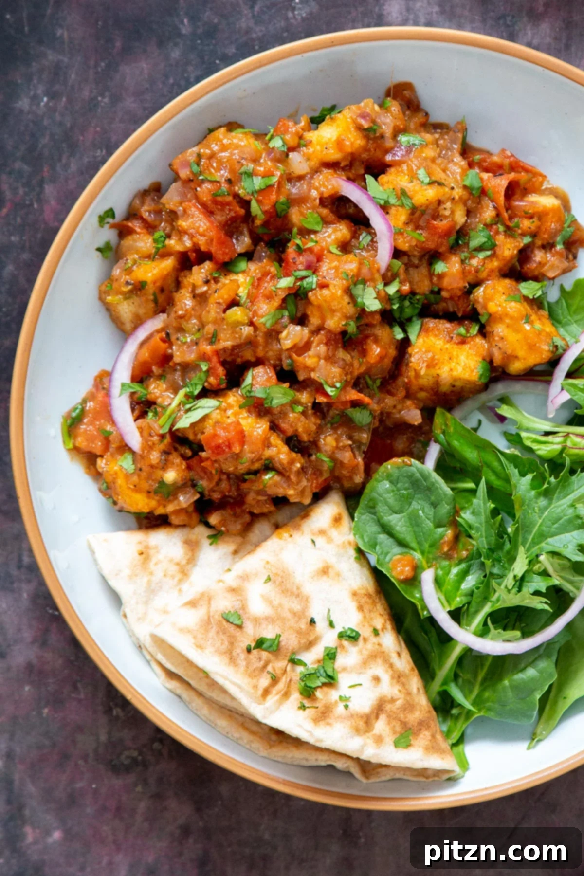 A beautifully plated serving of vegan Khada Masala Murg curry with tofu, accompanied by a vibrant side of fresh spinach and warm, fluffy flatbread.