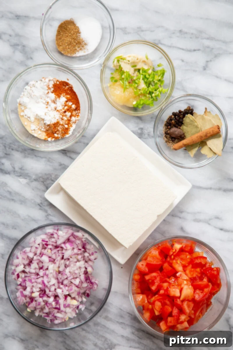 A collection of fresh ingredients laid out on a surface, including whole spices, tomatoes, onions, garlic, ginger, and tofu, ready for preparing Khada Masala Murg.