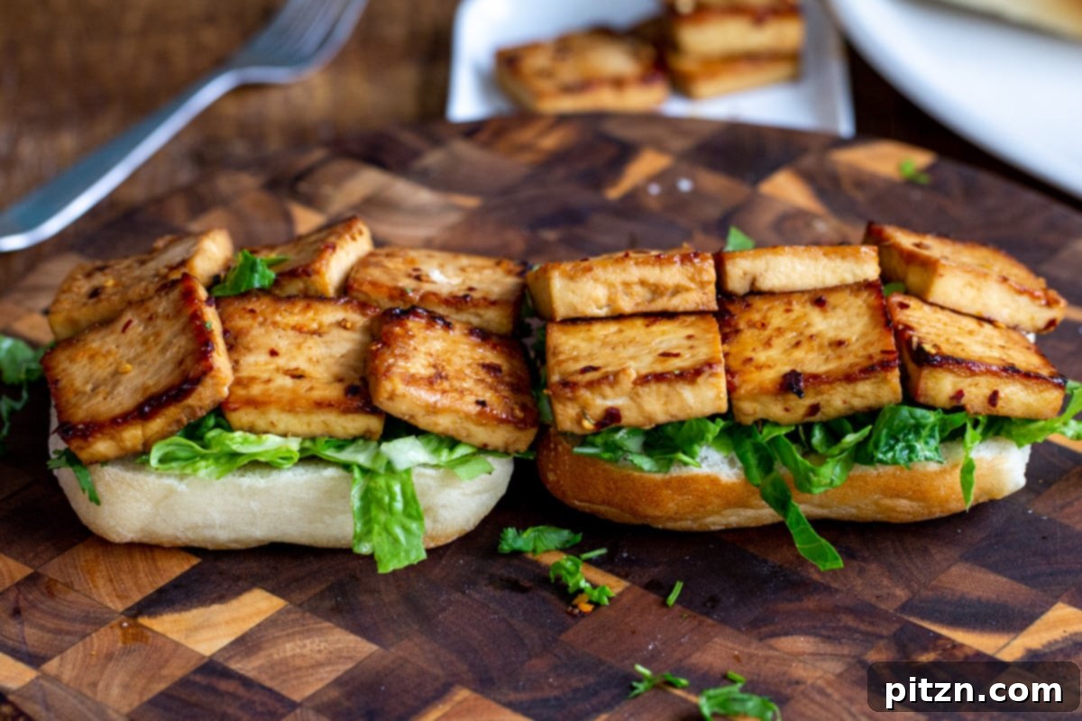 a sandwich being assembled with lettuce and baked chili garlic tofu