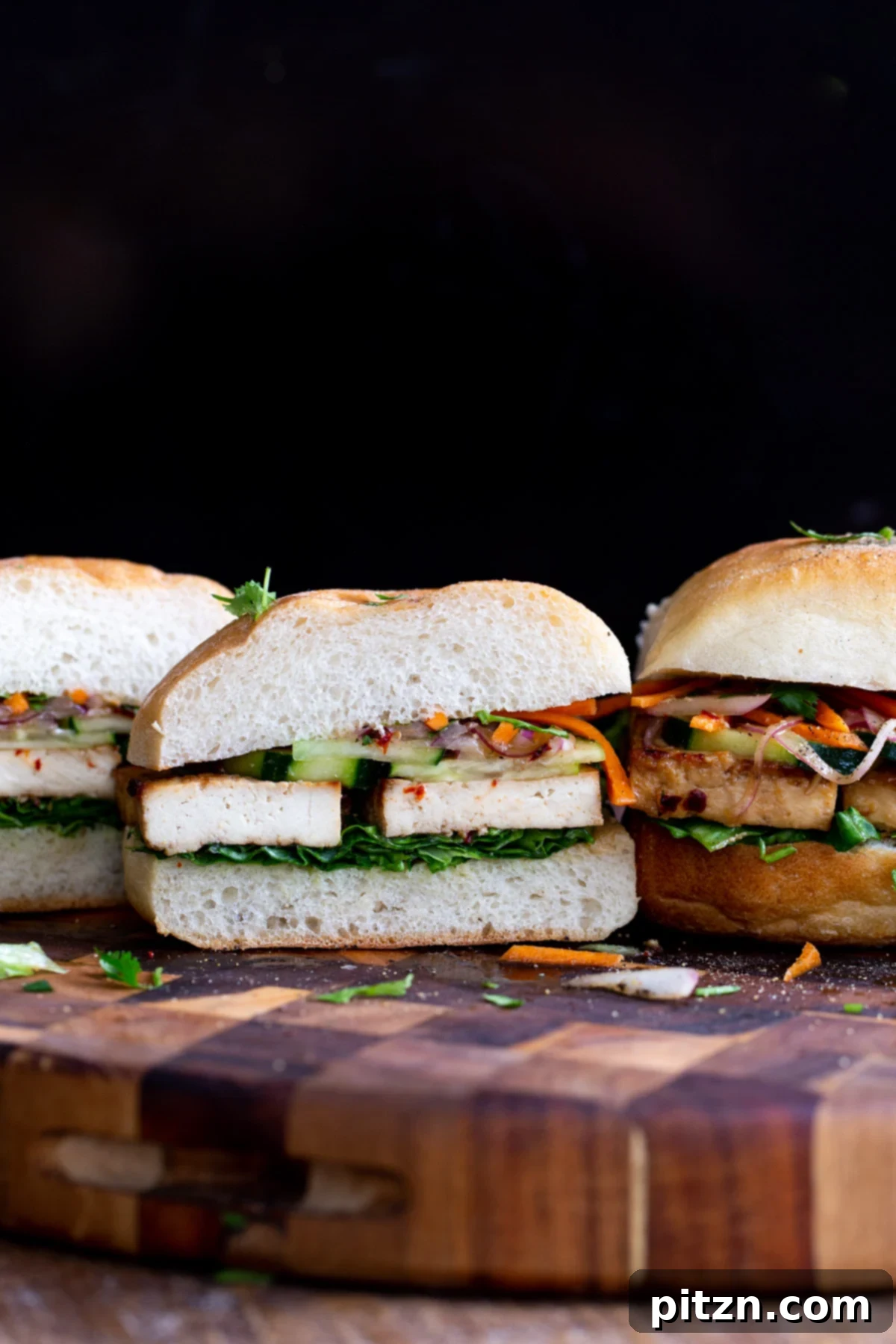 sliced vegan tofu sandwiches with chopped veggies on a wooden board