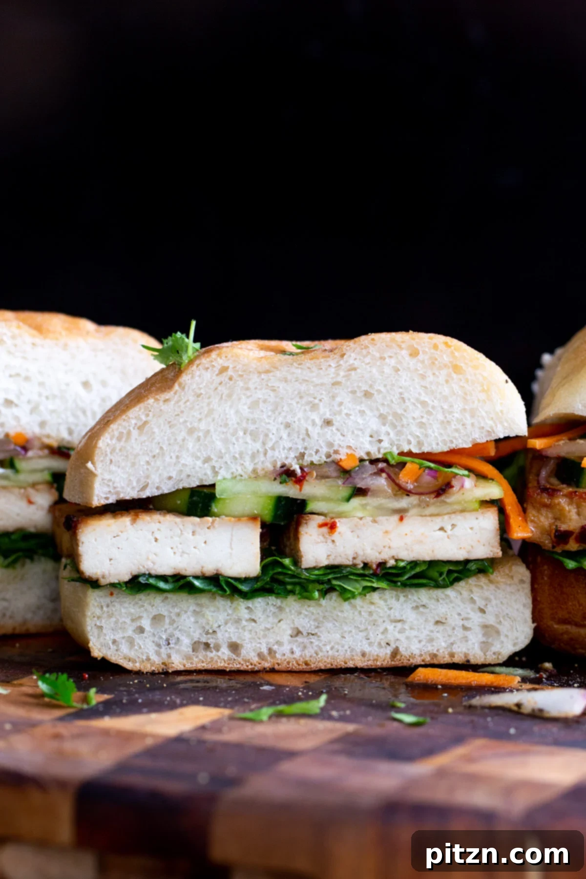 a vegan lunch sandwich sliced in the middle filled with baked tofu and topped with veggies