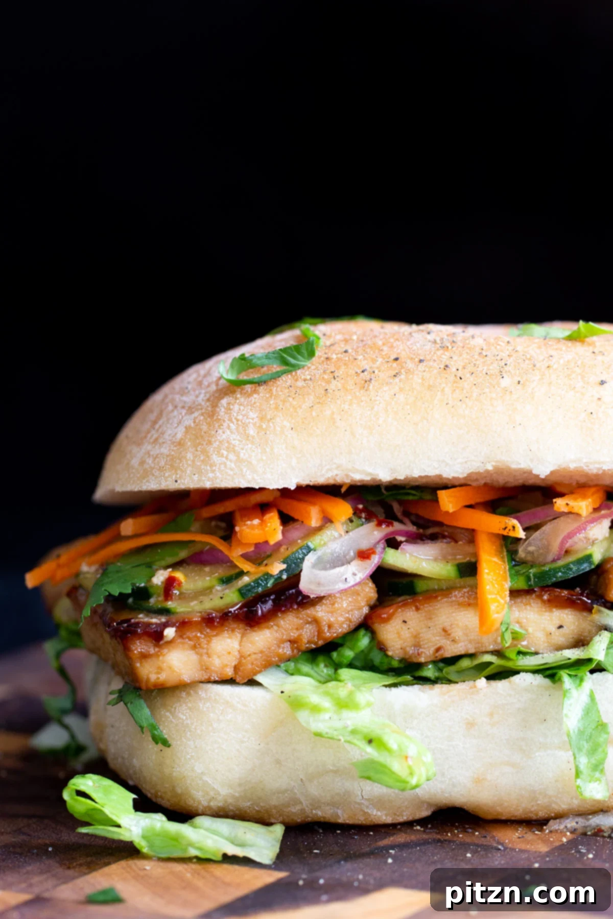 a vegan chili garlic tofu sandwich on a wooden chopping board being sliced in the middle
