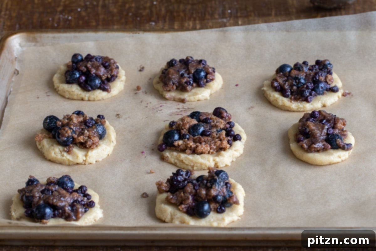 Gluten-Free Vegan Blueberry Muffin Cookies 15 Vegan Blueberry Muffin Cookies, topped with streusel, arranged on a lined baking sheet, ready for the oven. This Gluten-Free dessert is a visual delight.