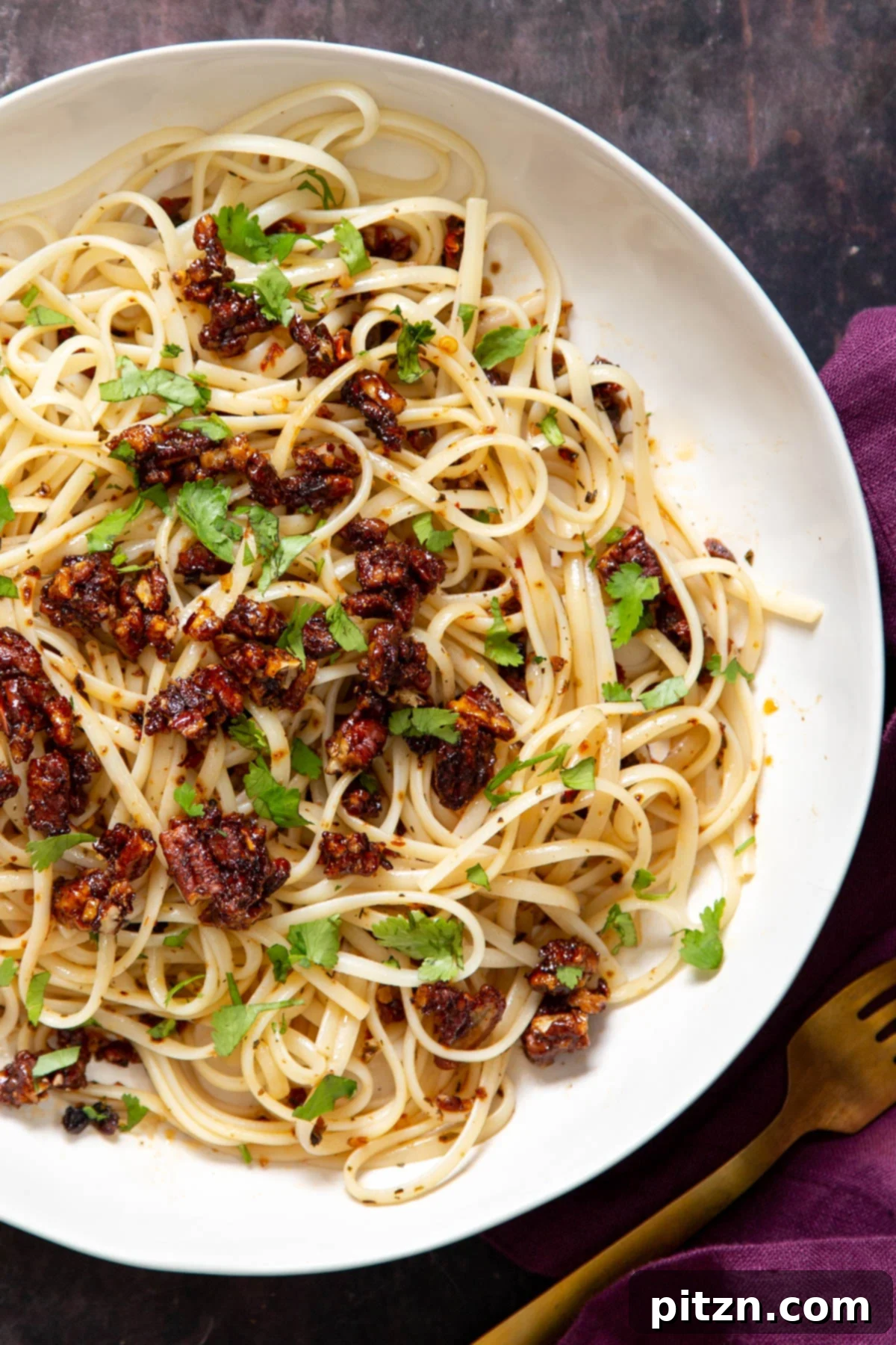 A vibrant plate of vegan garlic sun-dried tomato chili oil pasta, generously topped with candied pecans and fresh green herbs.