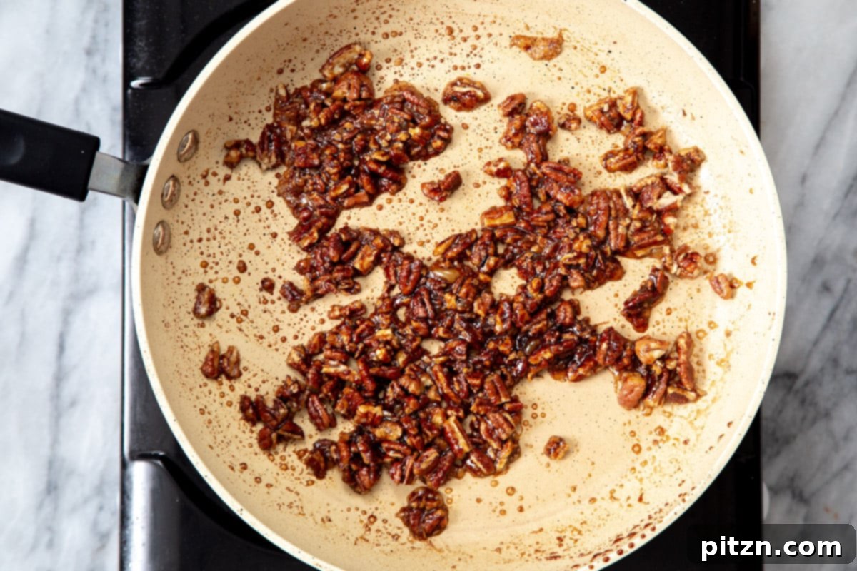 The perfectly candied pecans, coated in a smoky, savory, and sweet glaze, cooling in a sautéing pan after cooking.
