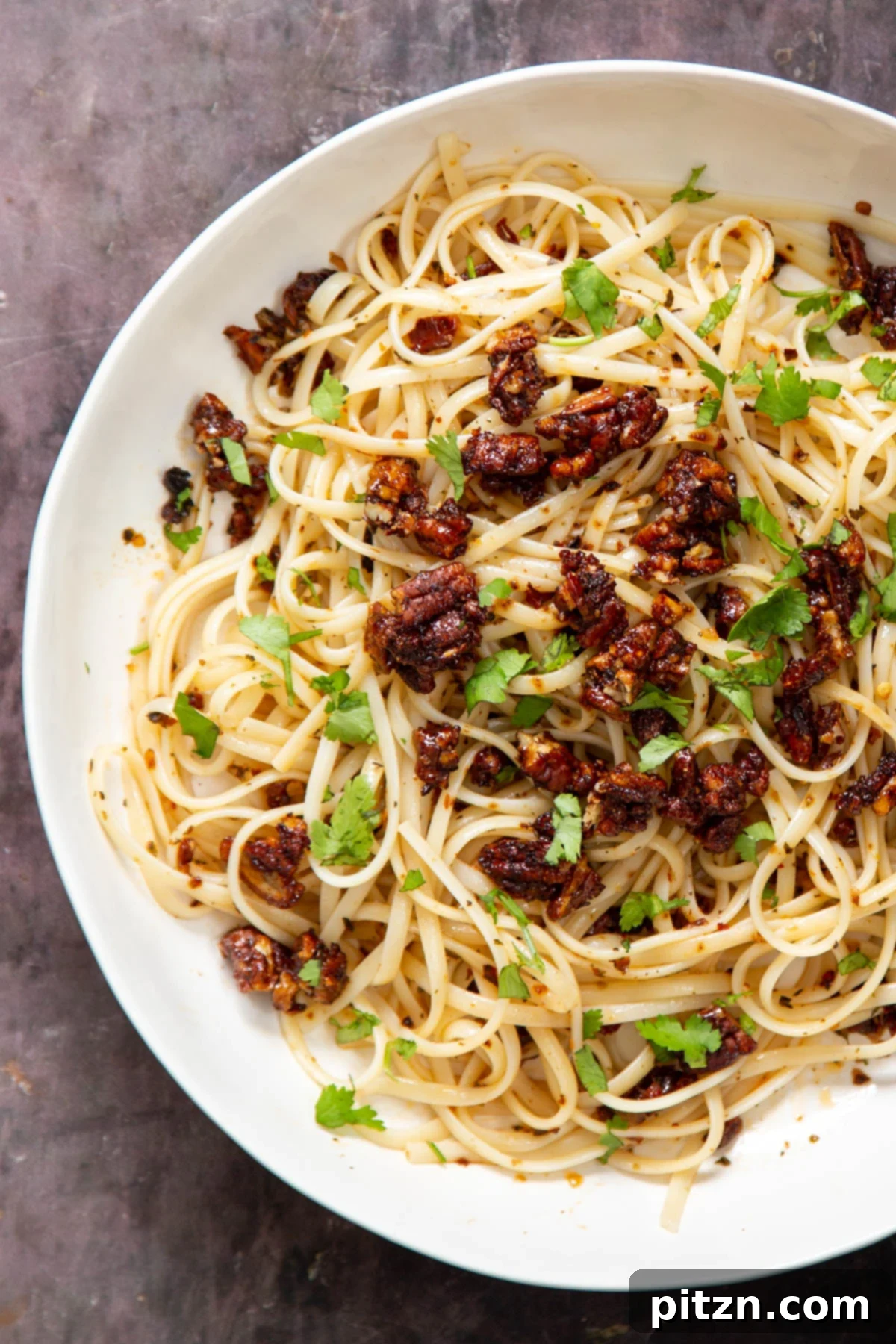 A beautifully plated bowl of vegan chili garlic oil pasta, adorned with a generous topping of candied pecans, ready to be served.