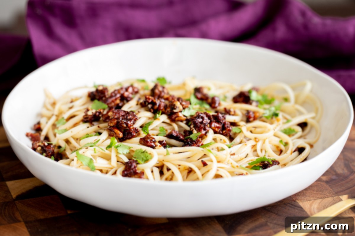 A wider shot of the vegan pasta with chili garlic oil and candied pecans, showcasing the full arrangement of the dish in a white bowl.
