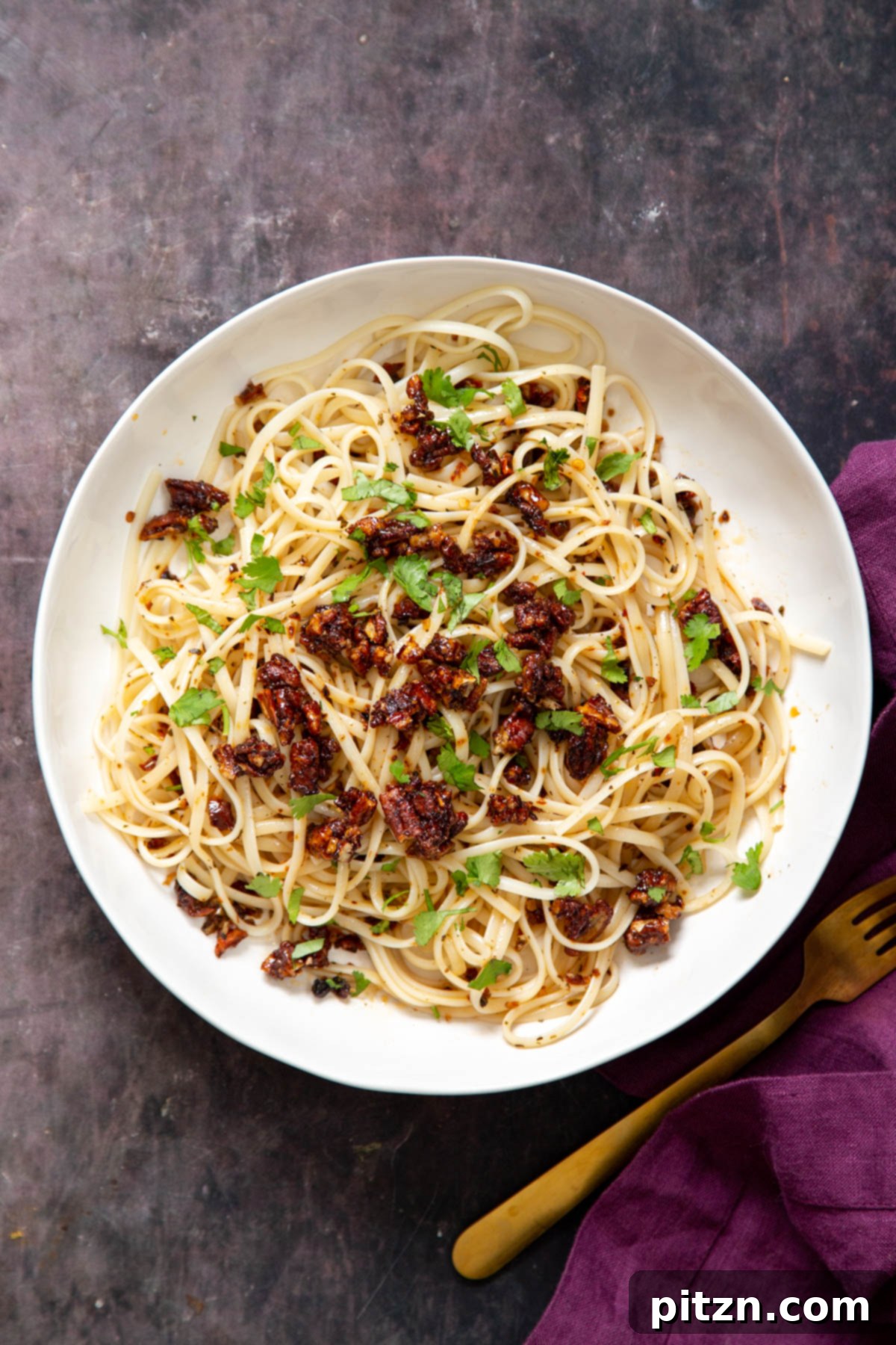 Close-up of vegan chili garlic oil pasta, beautifully arranged and sprinkled with candied pecans and fresh cilantro.