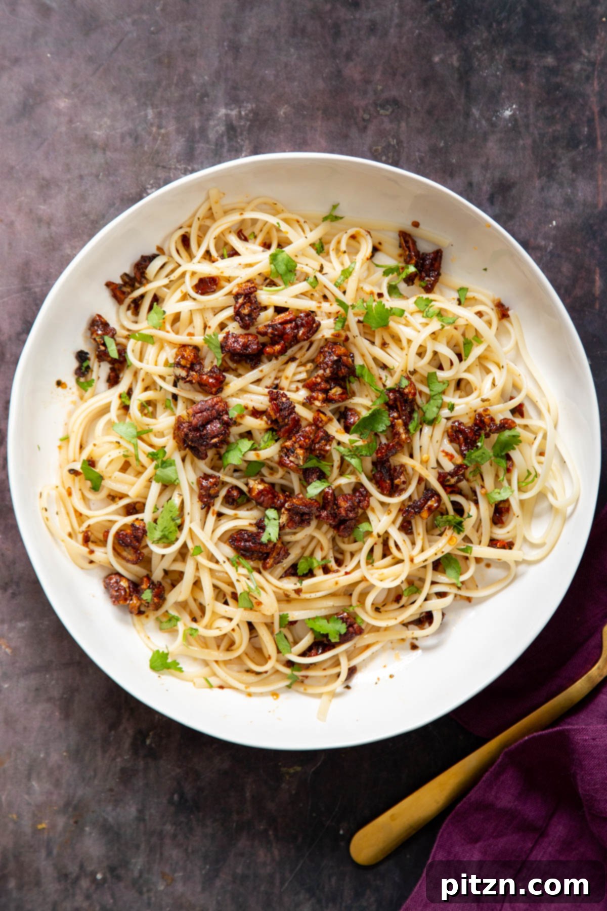 Overhead shot of a single serving of vegan chili garlic oil pasta, generously topped with smoky pecans in a modern white bowl.
