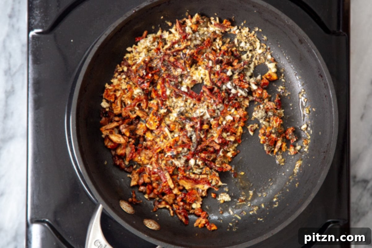 The vibrant vegan chili garlic oil mix simmering gently in a black sautéing pan, ready to be tossed with pasta.