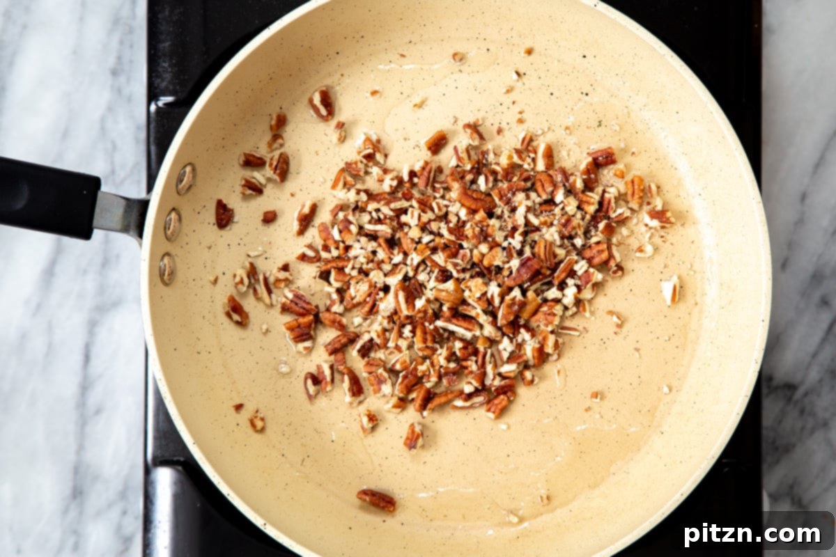 Chopped pecans being lightly toasted in a pan over medium heat, releasing their aromatic oils.