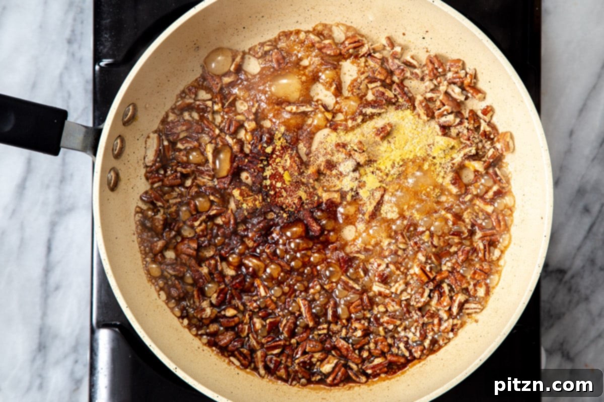 Toasted pecans caramelizing in a savory-sweet glaze of maple syrup, soy sauce, and a blend of spices in a pan.