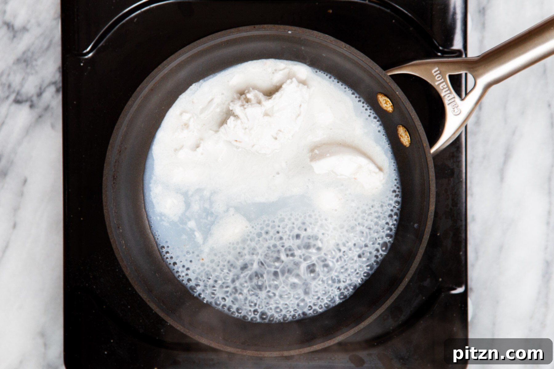 Decadent Mocha Swirl Cake 19 Full-fat coconut milk being gently heated in a small saucepan on a stove.