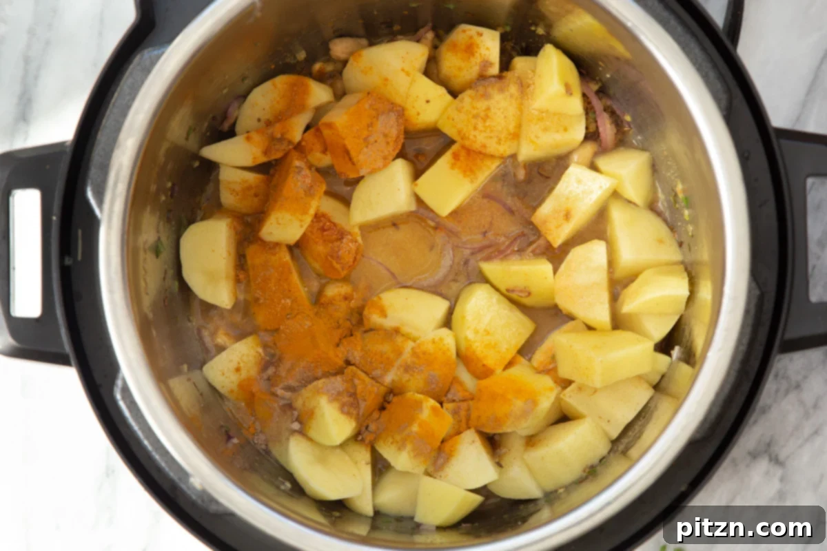 Cubed potatoes, spices, and liquid combined in an Instant Pot, ready for pressure cooking to create the samosa filling.