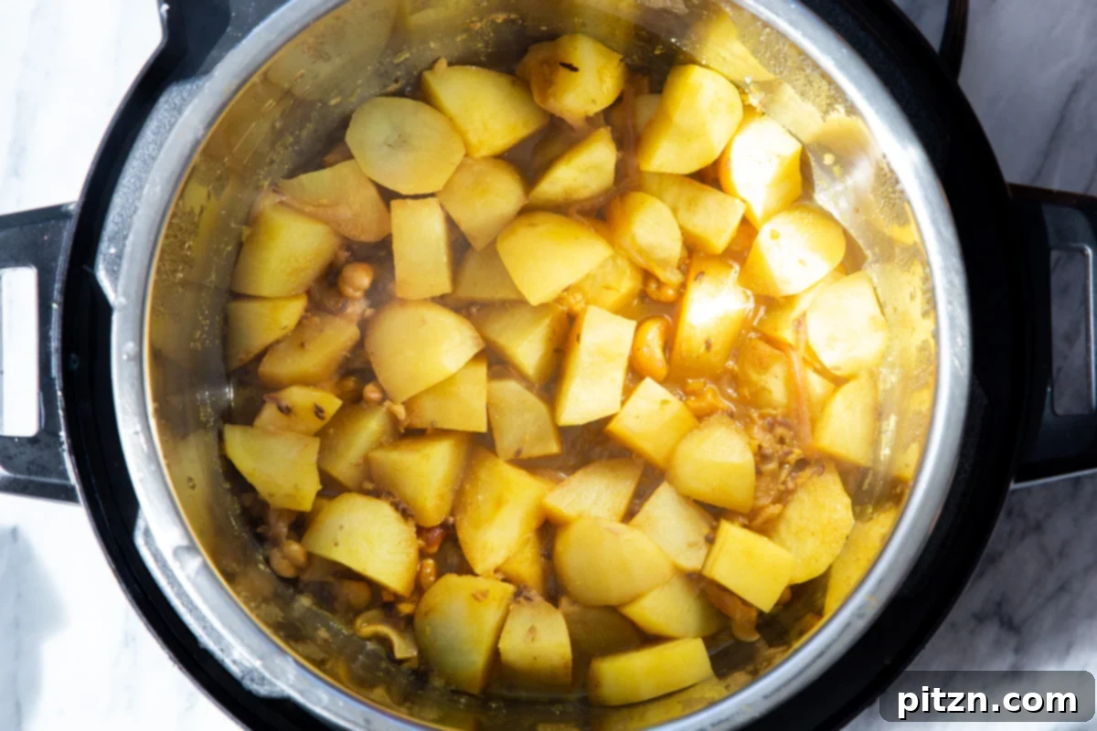Potatoes simmering with a rich blend of spices and cashews in an Instant Pot after pressure cooking, forming the delicious samosa filling.