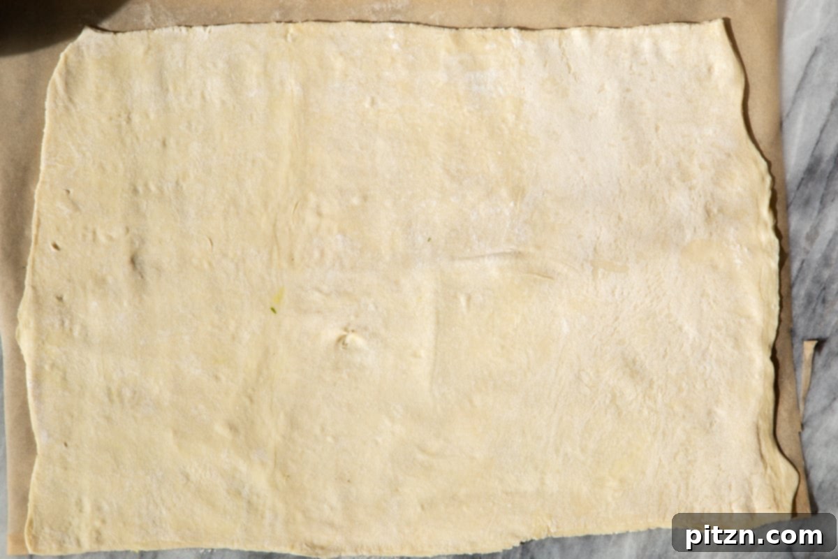 A thawed sheet of vegan puff pastry laid flat on a marble counter, ready for rolling and filling.