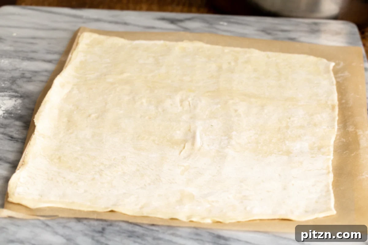 A rolled-out sheet of thawed puff pastry resting on baking paper, showing its increased size and readiness for the samosa filling.