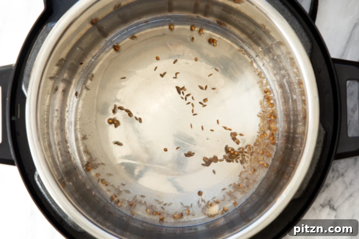 Cumin seeds sizzling in oil within an Instant Pot, starting the aromatic base for the samosa pie filling.