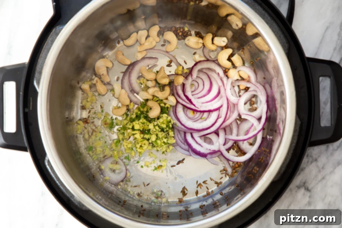 Chopped onions, ginger, garlic, cashews, and various spices sautéing in an Instant Pot, building layers of flavor for the samosa filling.