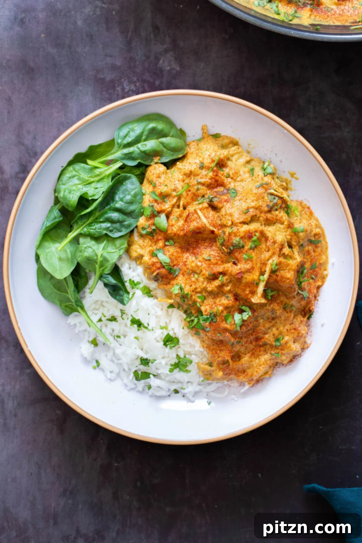 a serving of vegan chicken korma with jackfruit on a white plate served with rice and spinach 